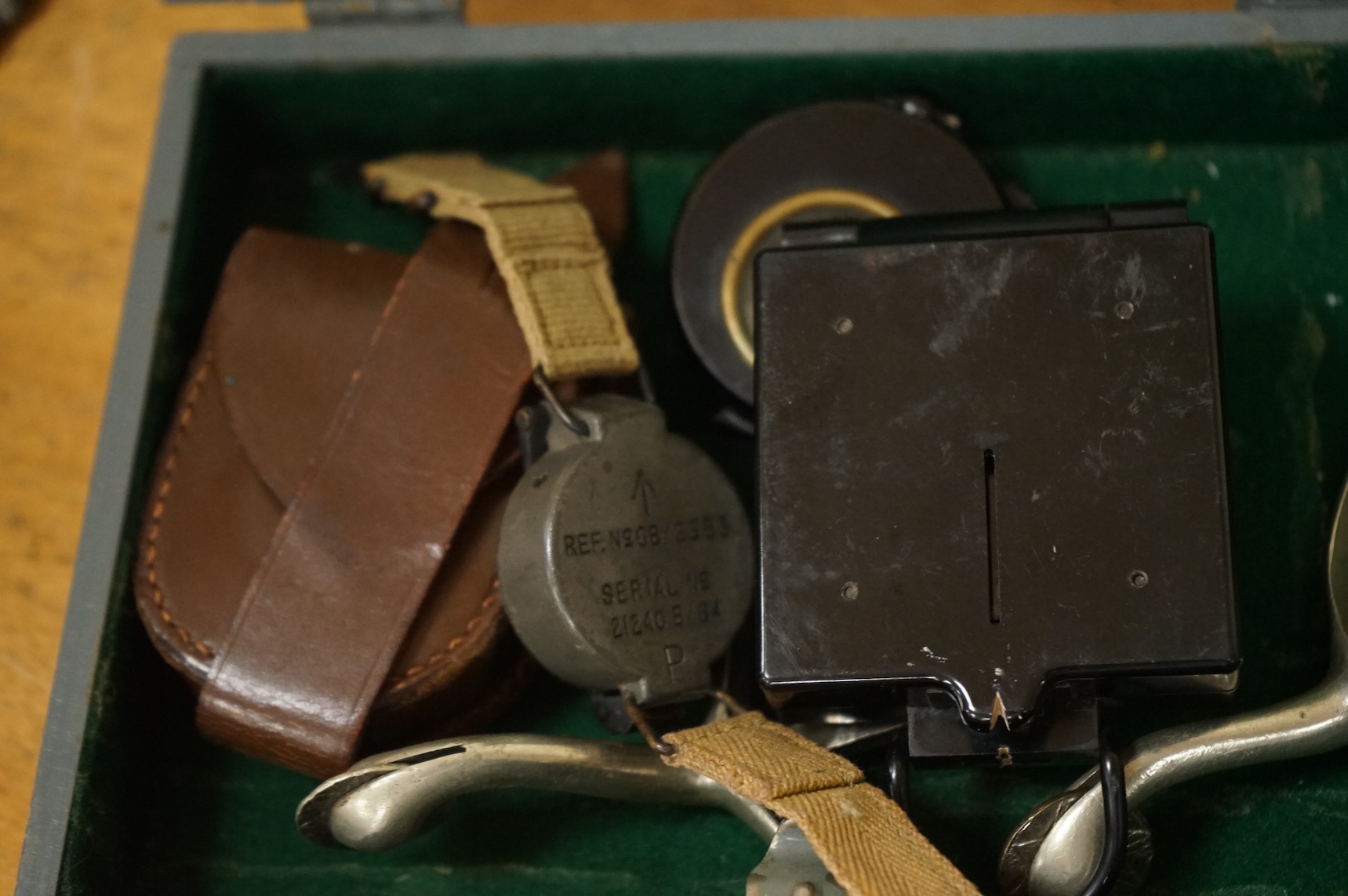 Three WWII military compasses including a Magnetic Marching Mark One compass, a small compass on a wrist strap and another in a leather case, together with a pair of steel spurs and a small grey painted wooden military b